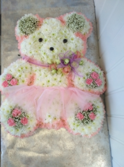 Teddy Bear Tribute - A teddy bear tribute with tutu and bow. Contains Spray Roses, Chrysanthemums, Gypsophila & Spray Carnations