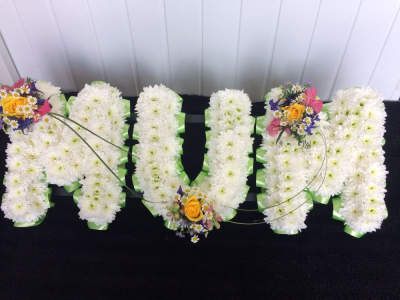 MUM - Yellow. Pink, Purple, Green & White - A MUM tribute in letters massed in white double chrysanthemums with a Yellow Rose & mixed flower cluster. Finished off with a green ribbon edge.