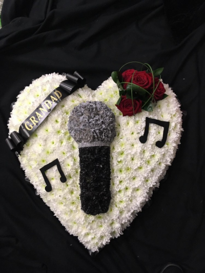 Microphone Tribute - A bespoke Microphone funeral tribute designed on a heart shaped pad. Finished off with musical notes, a red rose cluster and a ribbon sash. The name on the sash can be changed or removed all together.
