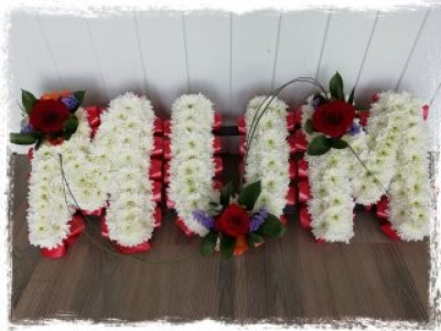 MUM - Red, White & Purple - A MUM tribute in letters massed in white double chrysanthemums with a Red Rose & mixed flower cluster. Finished off with a red ribbon edge.