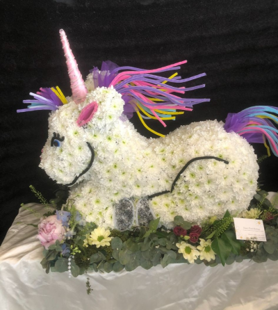 Unicirn - A 3 d unicorn in pretty pinks / whites surrounded by flowers and foliage .