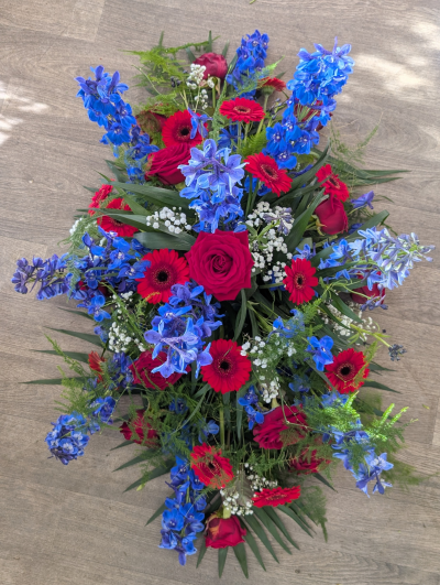 Casket Spray - Blue & Red - A beautiful casket spray filled with seasonal blooms in blues & red including roses & delphinium